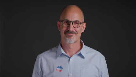 Studio-Portrait-Of-Mature-Man-Putting-I-Voted-Sticker-On-Shirt-In-American-Election